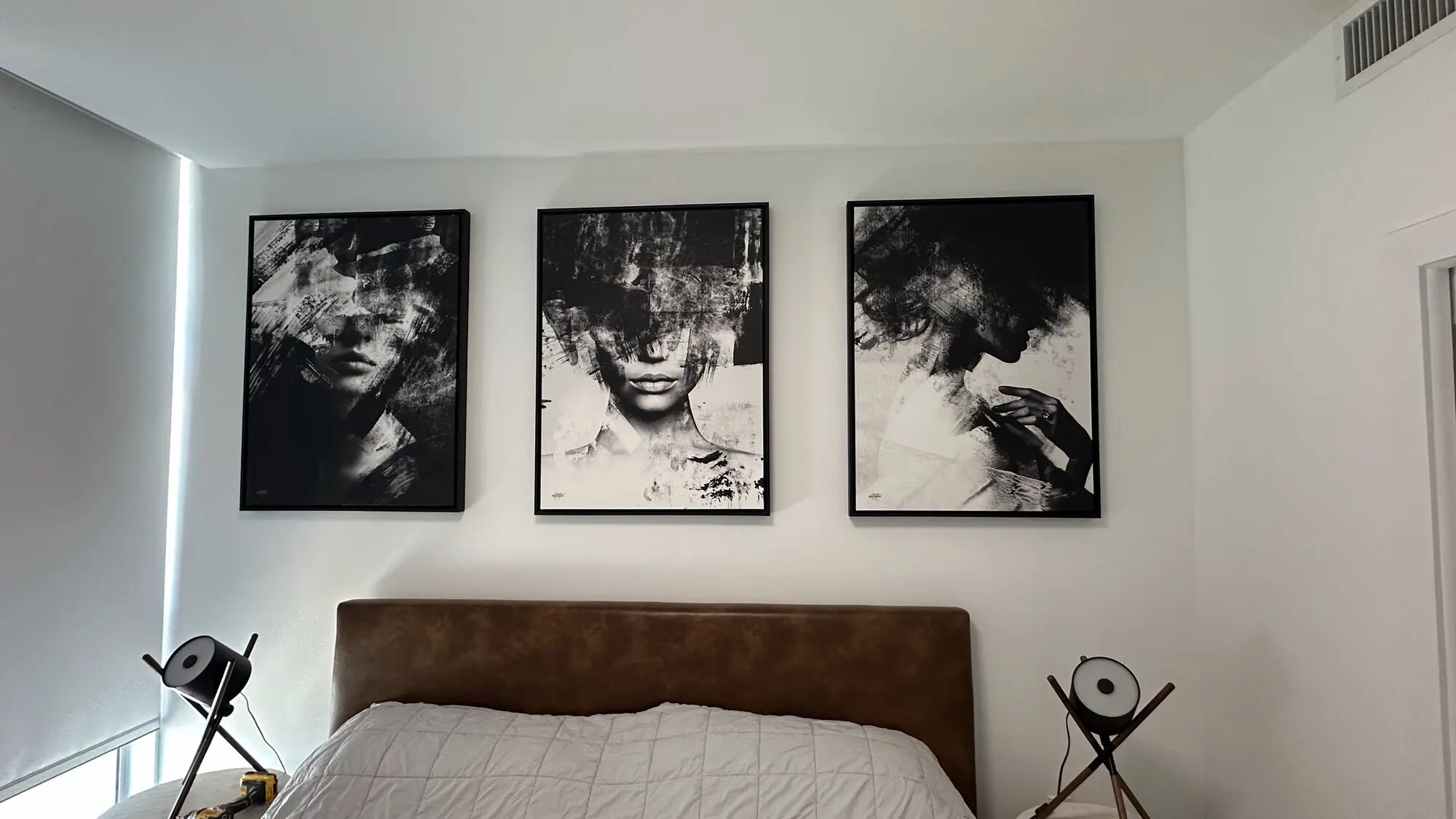 Three large framed art panels hung above an upholstered bed
