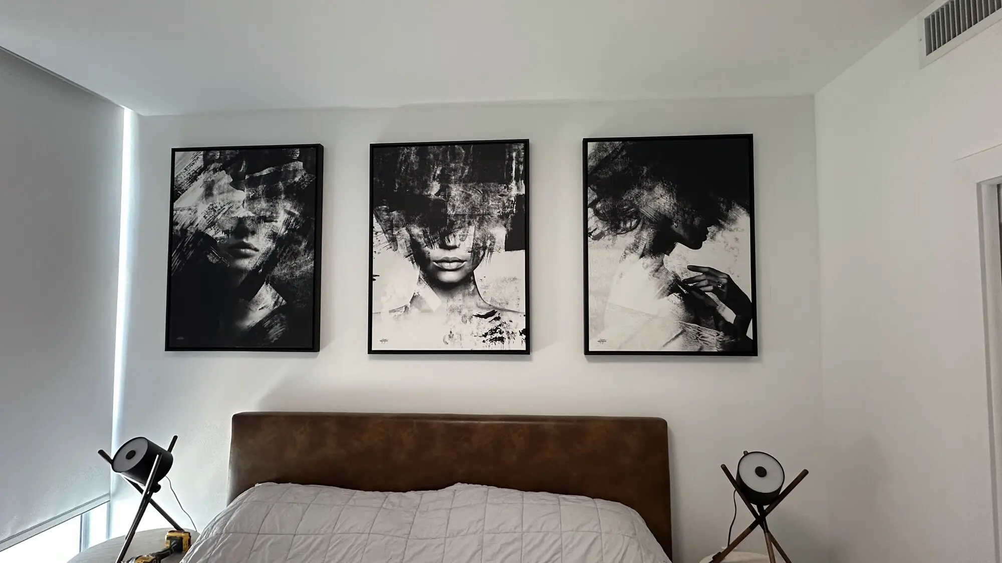 Three large framed art panels hung above an upholstered bed