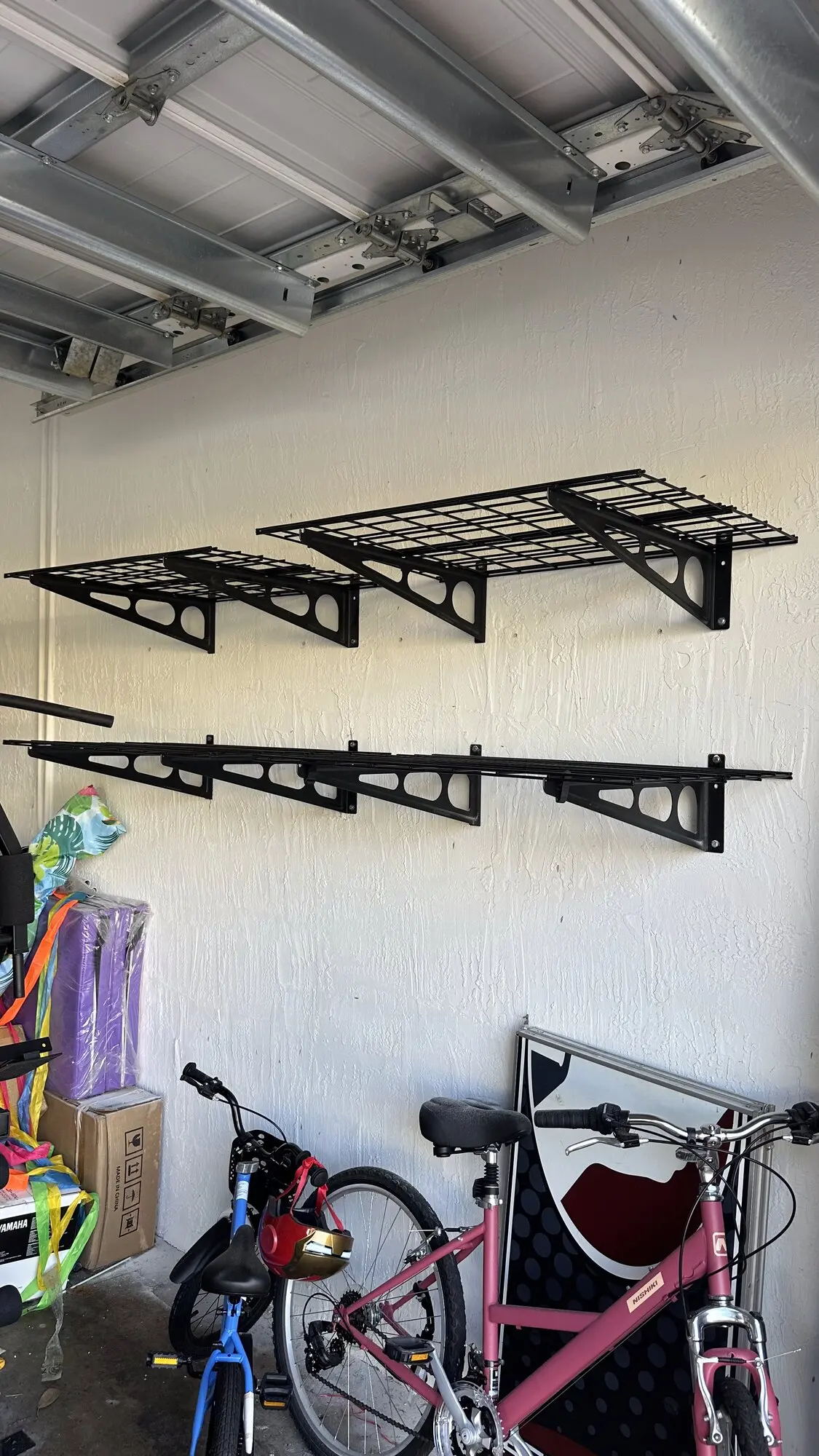 Two black overhead garage storage racks installed on a garage ceiling above bicycles