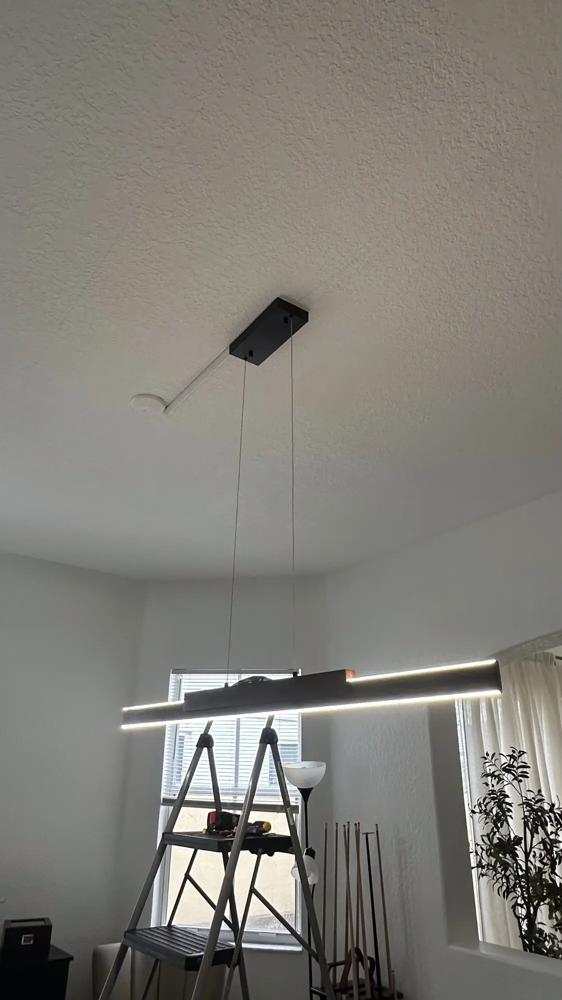 Linear pendant light suspended over a stairwell with a ladder in position