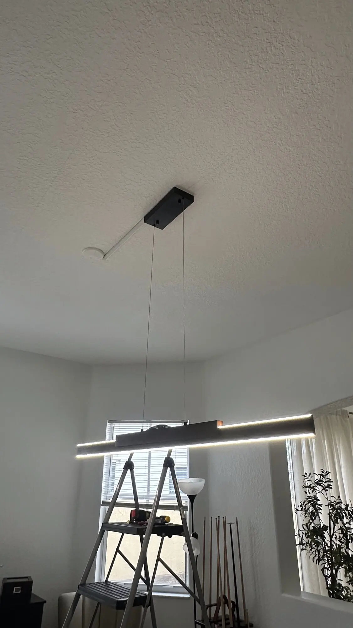 Linear pendant light suspended over a stairwell with a ladder in position