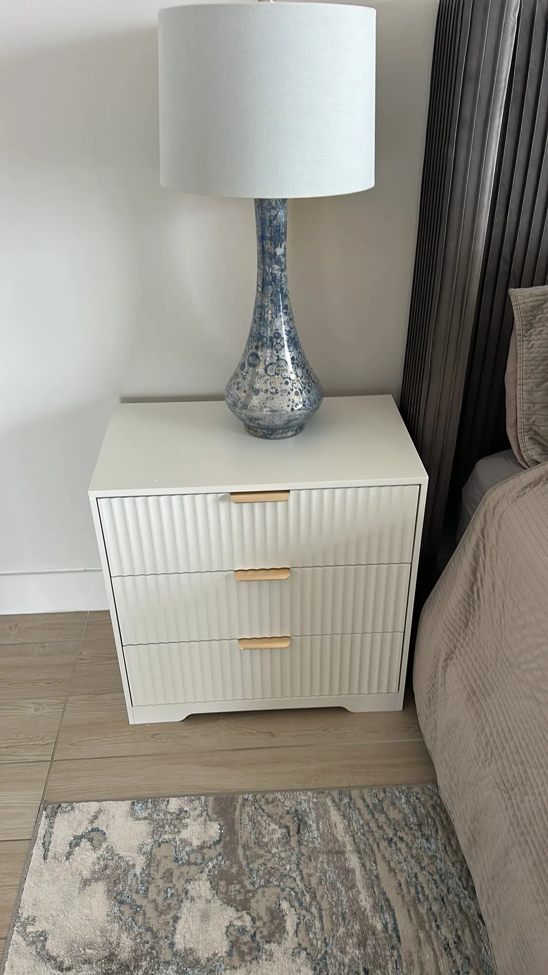 Fluted white nightstand assembled beside a bed with a table lamp on top