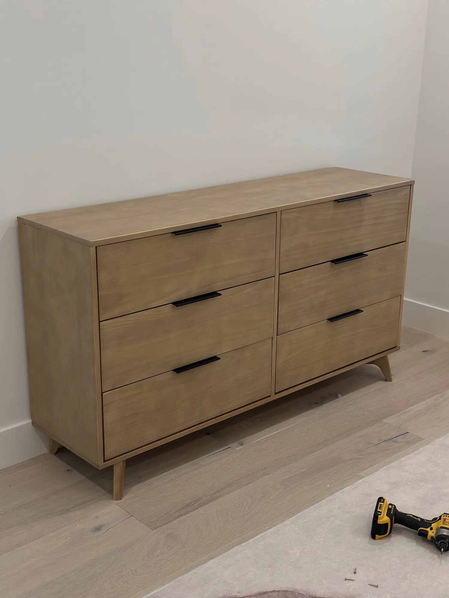 Six-drawer oak dresser assembled in a bedroom with a cordless drill on the floor