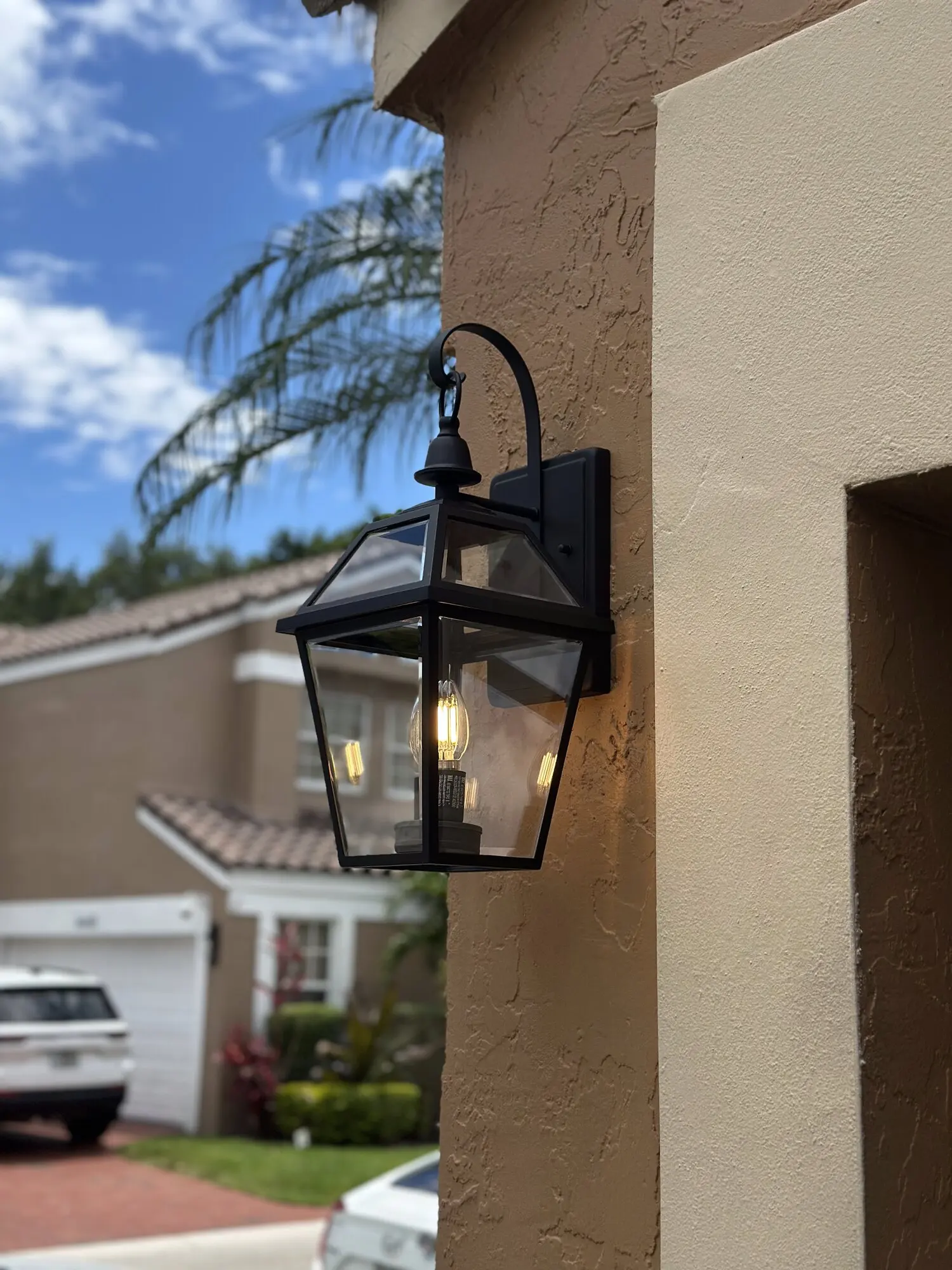 Black outdoor lantern wall light installed beside a garage on a South Florida home